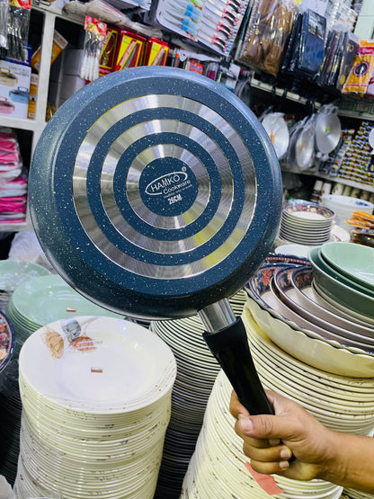 Blue frying pan with a black handle held above stacks of plates in a store setting